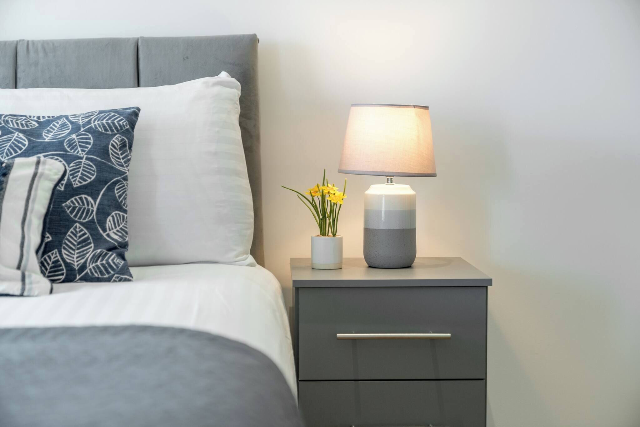 A neatly made bed with a pillow, a bedside lamp, and a small vase with flowers.