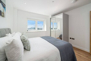 A bedroom with a bed, a window, a mirror, and a door. - Skyvillion-apartments Near River Thames Excel & O2 Woolwich (London)