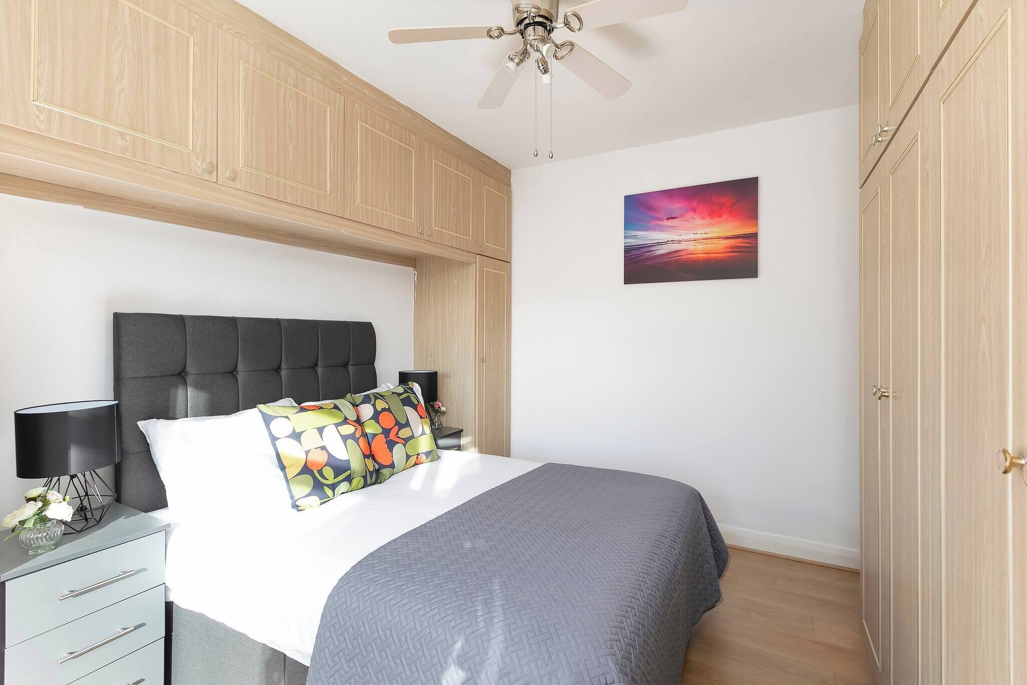 A bedroom with a bed, a nightstand, a ceiling fan, and a wardrobe.