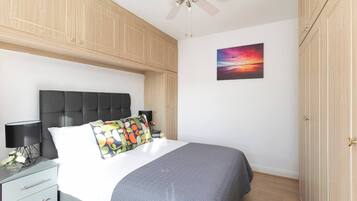 A bedroom with a bed, a nightstand, a ceiling fan, and a wardrobe.