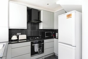 A modern kitchen with white cabinetry, a black stove, a microwave, and a refrigerator. - Skyvillion - Enfield 4bed House W Garden & Parking (Enfield)