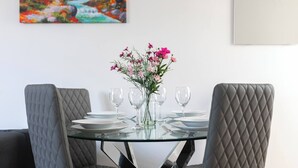 A dining table with a glass top, surrounded by four grey upholstered chairs with quilted backs. - Skyvillion - Enfield 4bed House W Garden & Parking (Enfield)