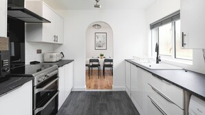 A modern kitchen with white cabinets, a black countertop, a stove, and a window. - Skyvillion - 3bed Home W Grdn For A Family Getaway (Stevenage)