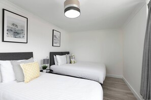 Une chambre d’hôtel avec deux lits, un luminaire au plafond, des œuvres d’art encadrées au mur et une table de chevet avec une lampe.