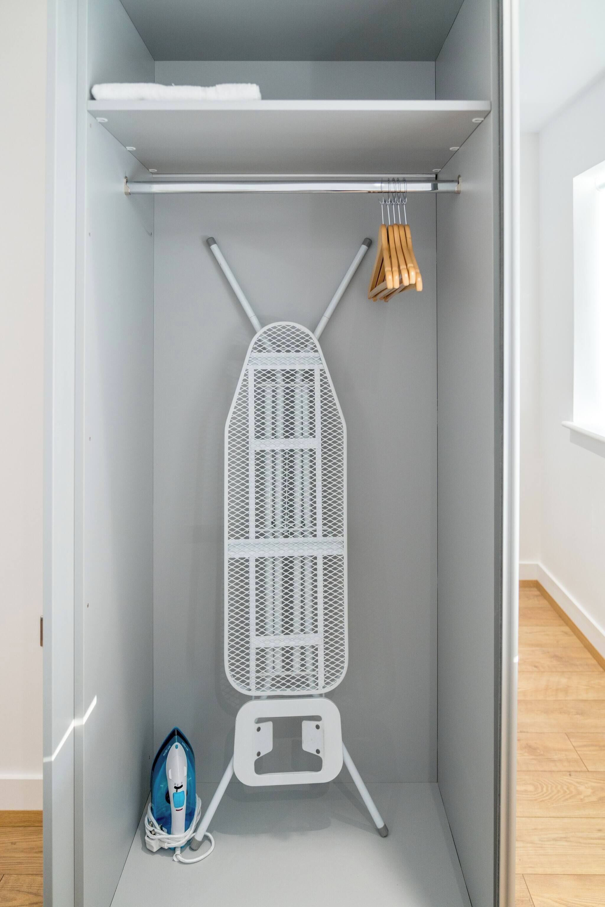 A compact room with a built-in ironing board, a hanging rack, and a portable iron.