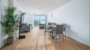 A modern living room with a sofa, dining table, chairs, a TV, and a large window.