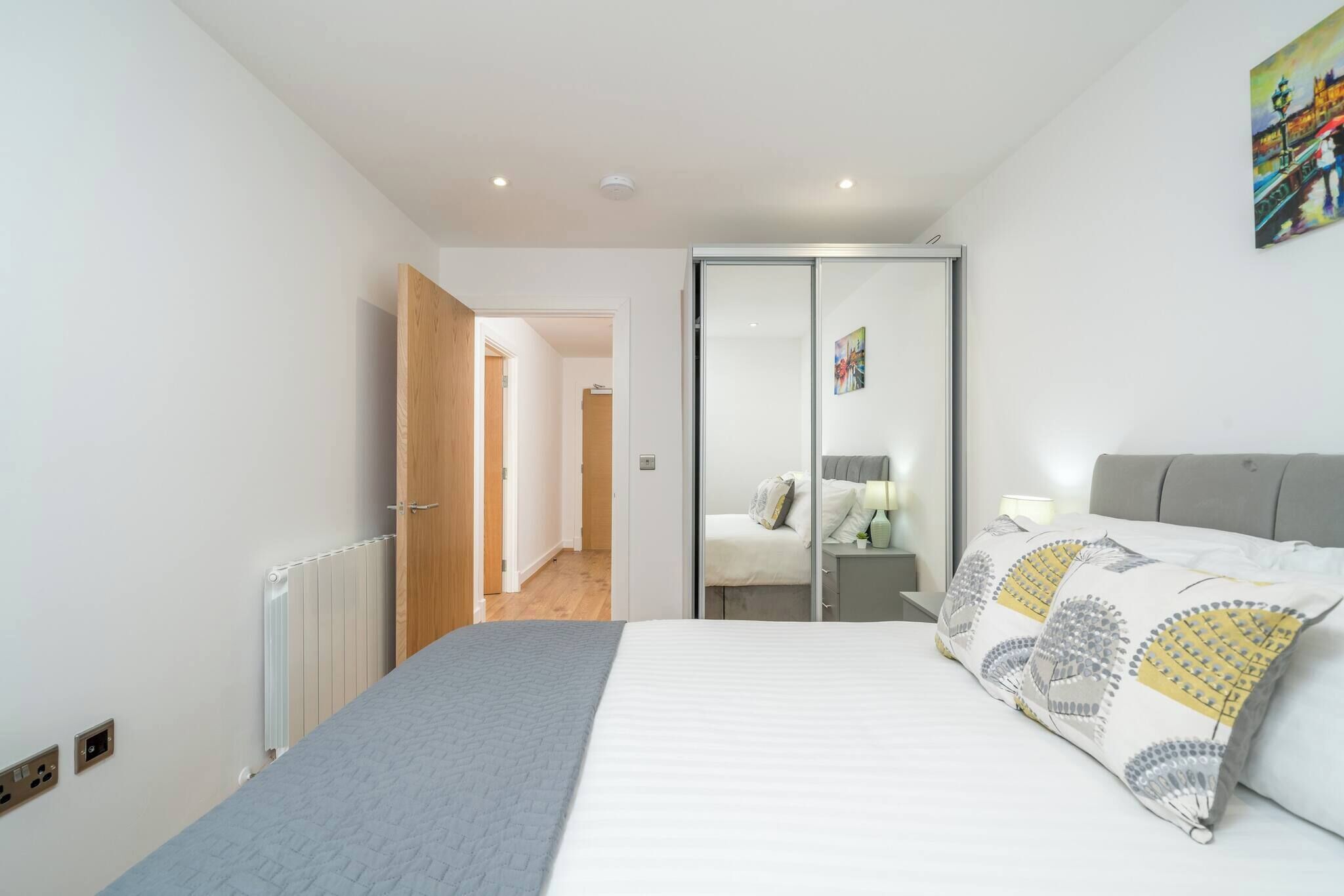 A bedroom with a bed, a radiator, a door, and a painting on the wall.