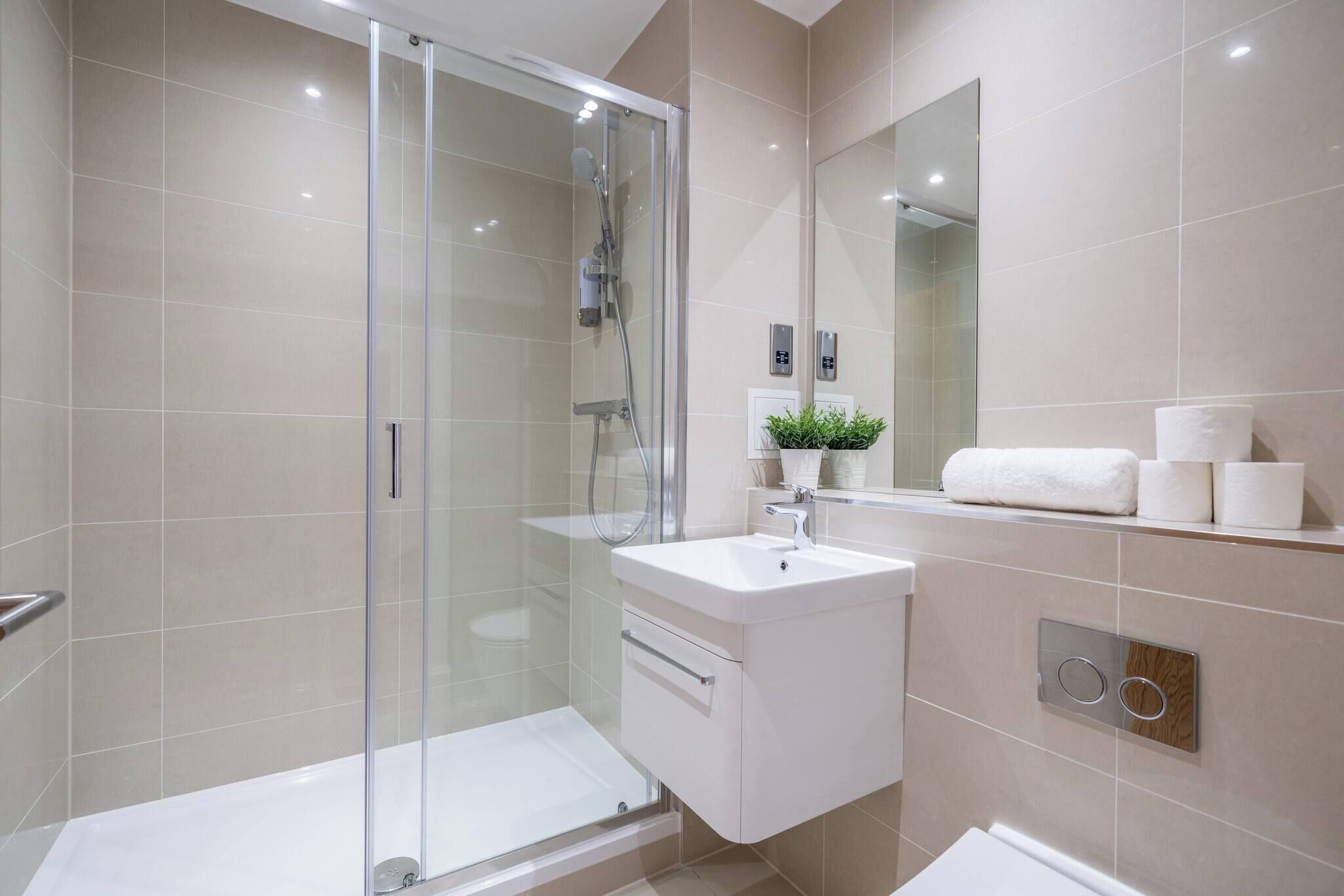 Une salle de bain moderne avec une douche à parois de verre, un lavabo blanc et un miroir au-dessus du lavabo.
