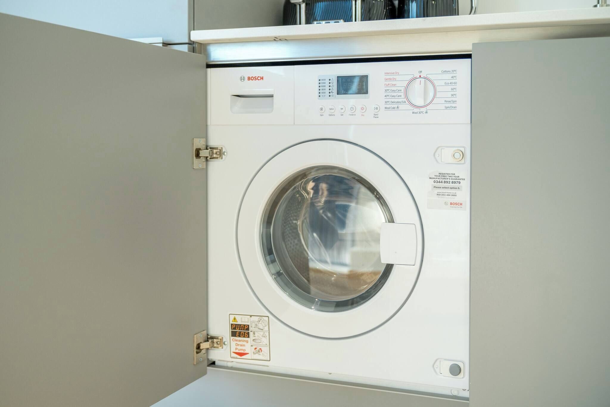 Een Bosch wasmachine met een digita bedieningspaneel, een voorlaadklep en een veiligheidswaarschuwing.