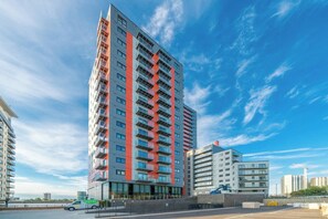 Ein Hochhaus mit mehreren Balkonen, einem Parkplatz und blauem Himmel.