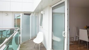 A balcony with a glass railing, a white chair, and a dining area with chairs and a table. - Skyvillion - Tower Point Enfield 1bed With Balcony (Enfield)