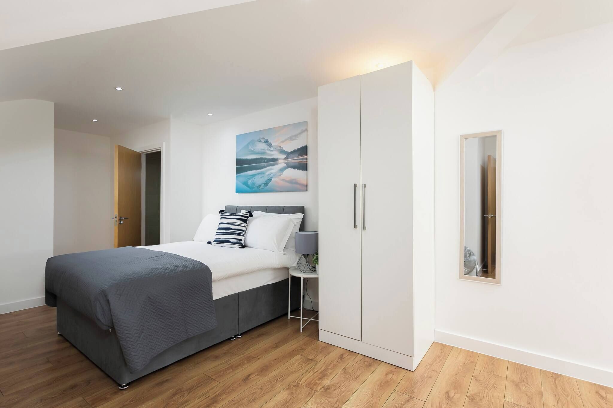 A modern bedroom with a bed, a nightstand, a wardrobe, and a painting on the wall.