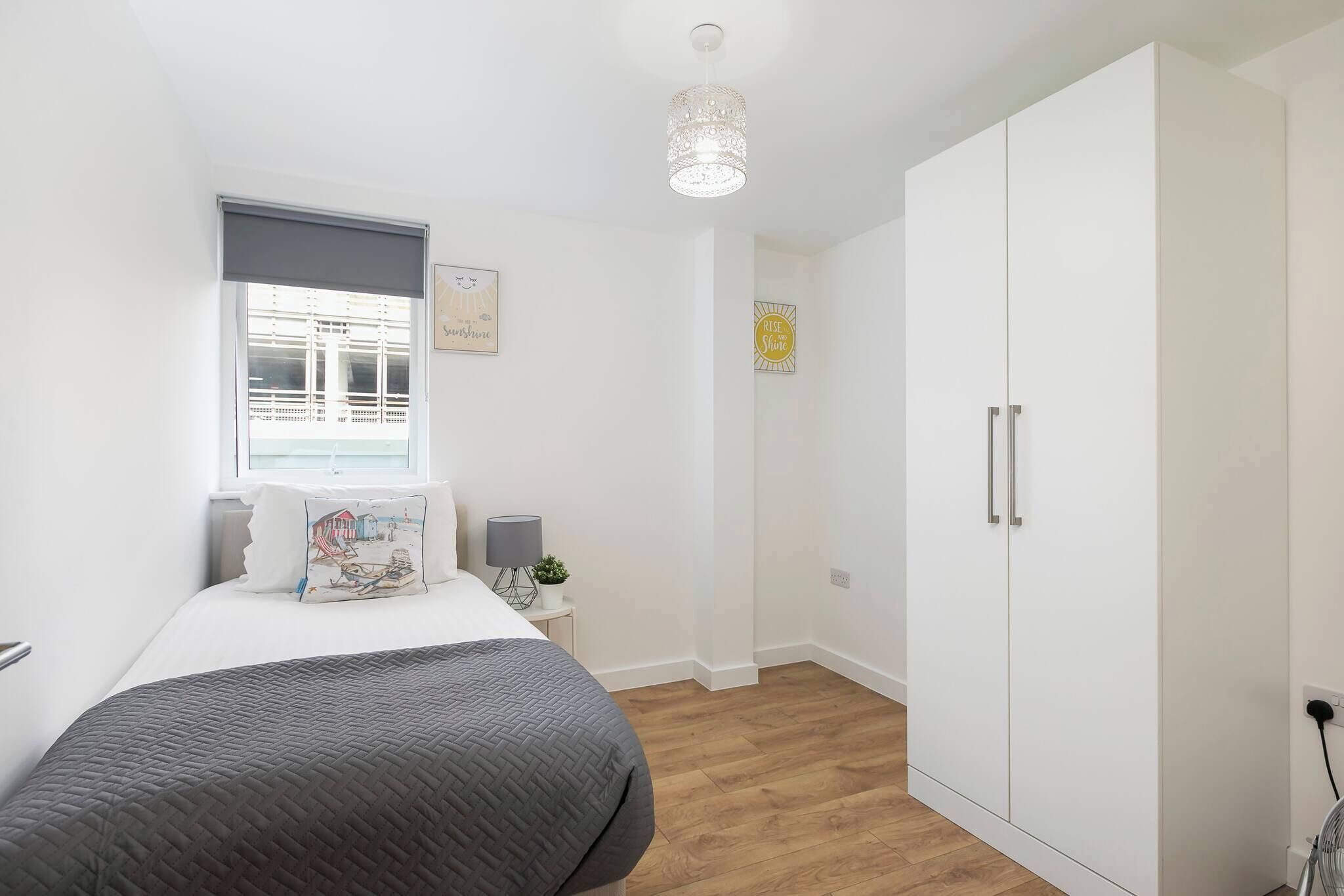 Ein Schlafzimmer mit Bett, Schrank, Nachttisch, Lampe, Fenster und Wanddekoration.