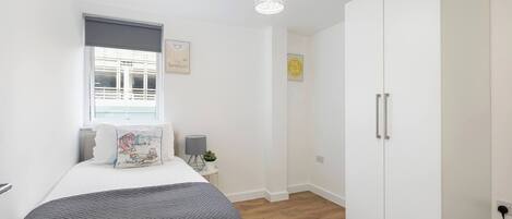 Ein Schlafzimmer mit Bett, Schrank, Nachttisch, Lampe, Fenster und Wanddekoration.