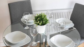 A round glass table with white plates, clear wine glasses, and a small potted plant. - Skyvillion - Huge 4bed Apartment Wbalcony - Parking (Enfield)