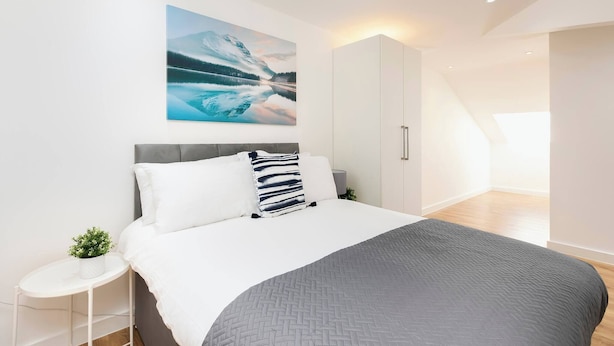 A modern bedroom with a bed, a nightstand, a potted plant, and a large window. - Skyvillion - Huge 4bed Apartment Wbalcony - Parking (Enfield)