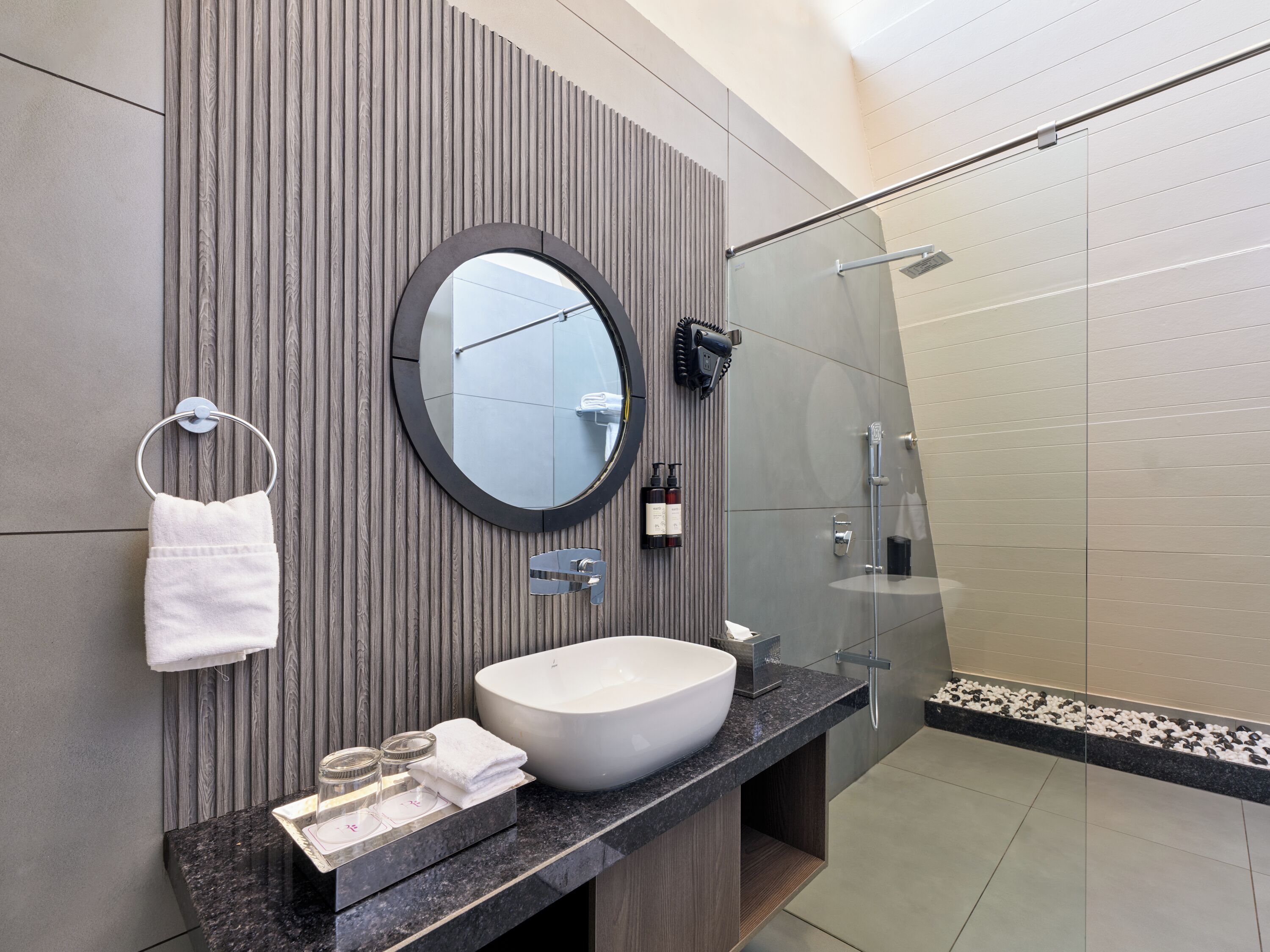 A modern bathroom with a large oval mirror, a white sink, and a glass shower enclosure.