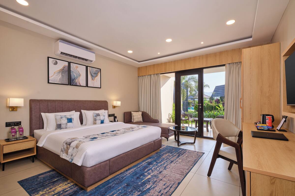 A hotel room with a large bed, a desk, a chair, a TV, and a view of the outdoors.