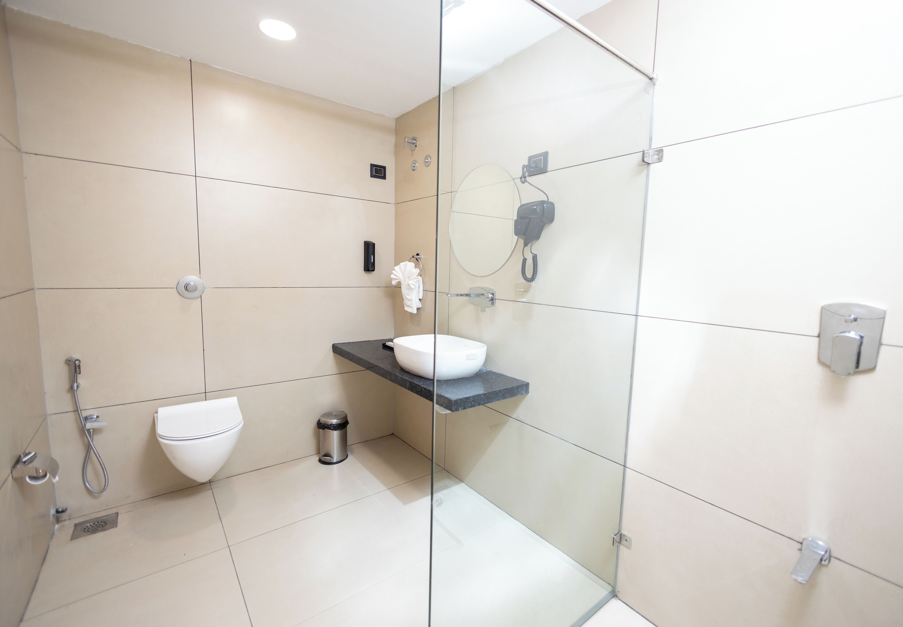 Een moderne badkamer met een douchecabine van glas, een wit toilet, een wastafel met een zwart aanrechtblad en een spiegel met een telefoon.