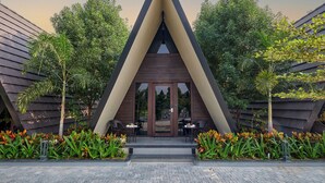 A modern building with a triangular facade, surrounded by lush greenery and outdoor seating.