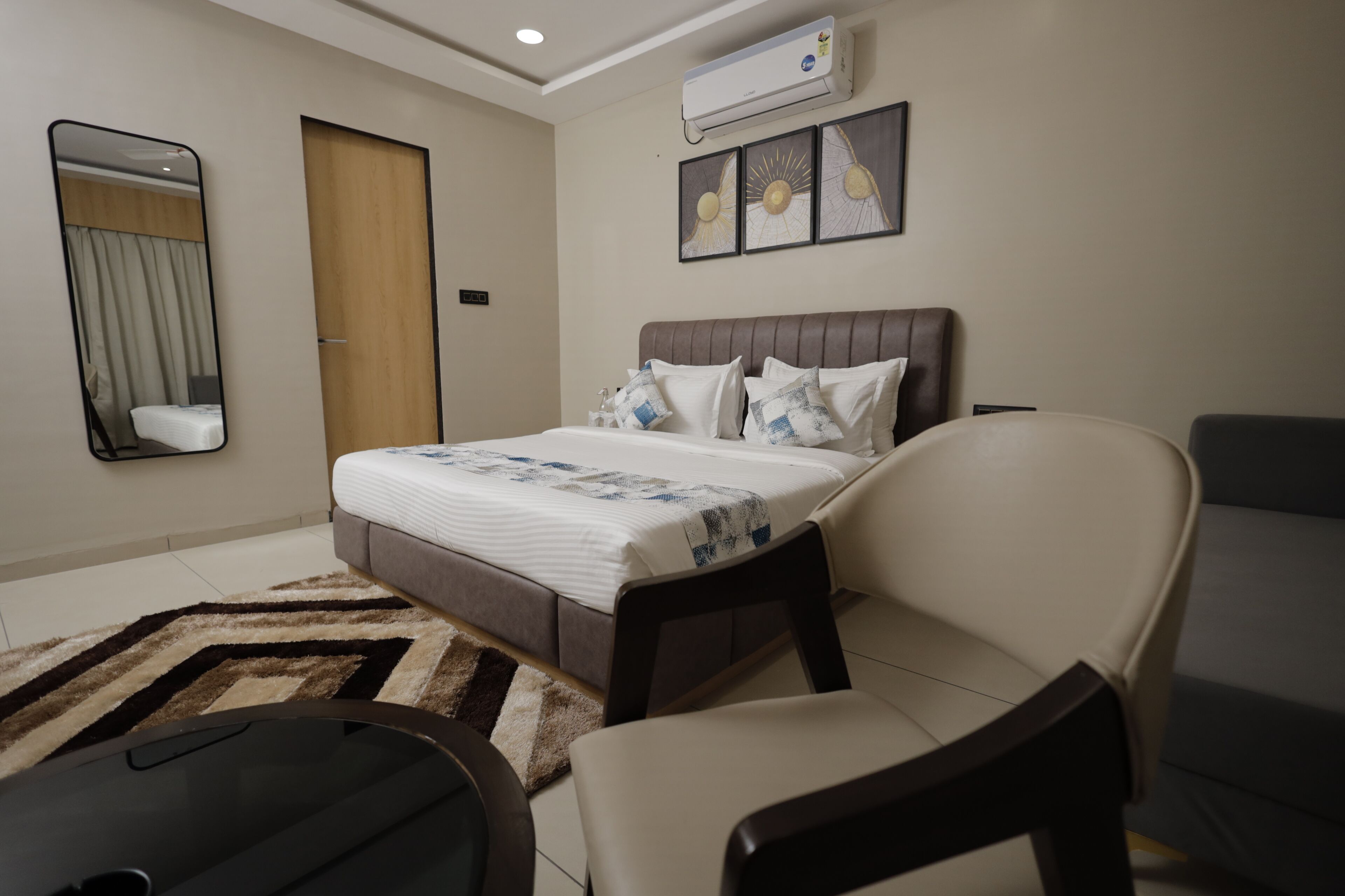 Una habitación de hotel moderna con una cama, un sillón, un sofá, un espejo y un equipo de aire acondicionado.