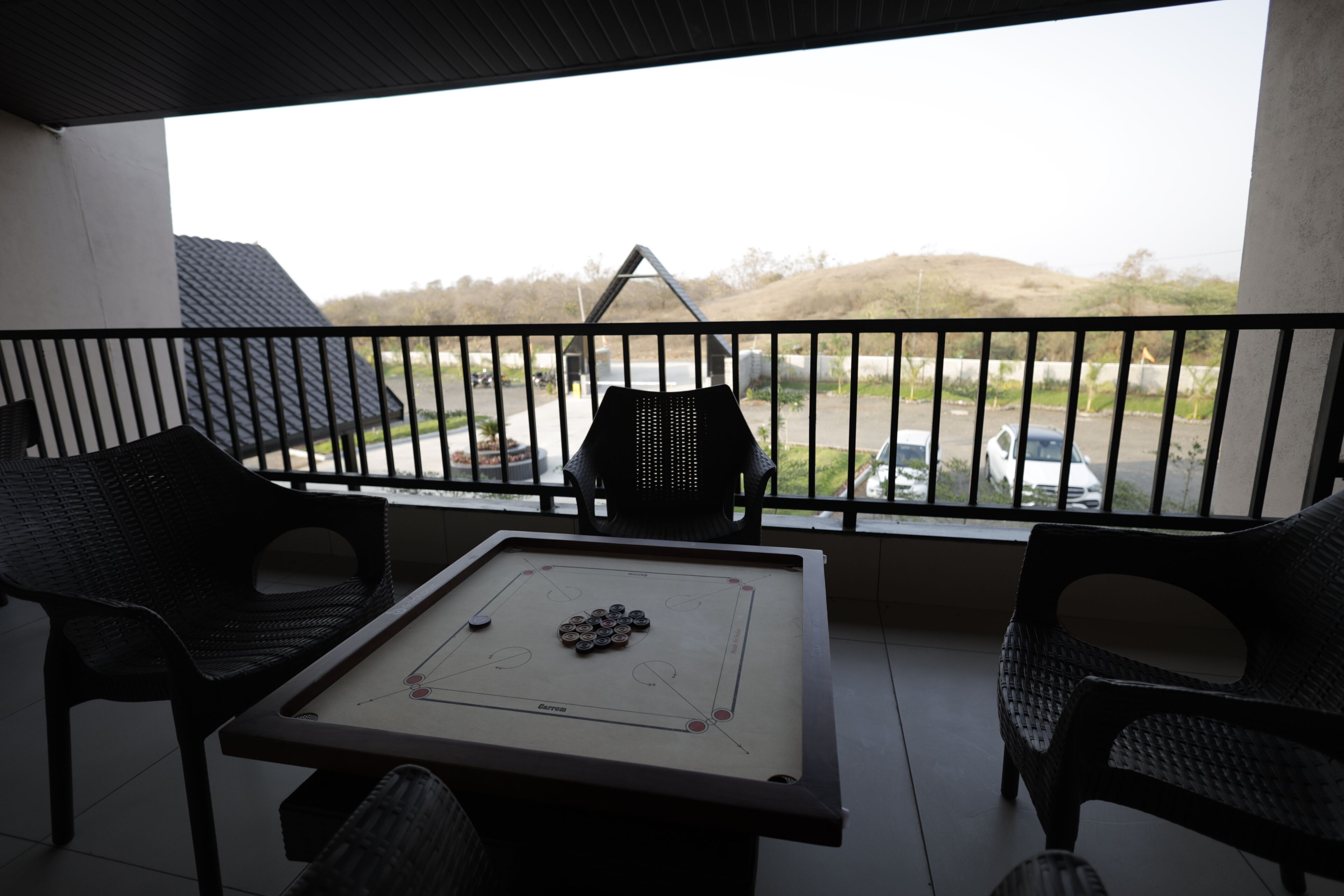 Een balkon met een biljart, twee stoelen en uitzicht op een parkeerplaats en heuvels.