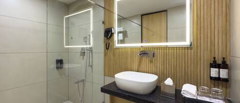 Un baño moderno con ducha de vidrio, un espejo grande, un lavabo blanco y paneles de madera.