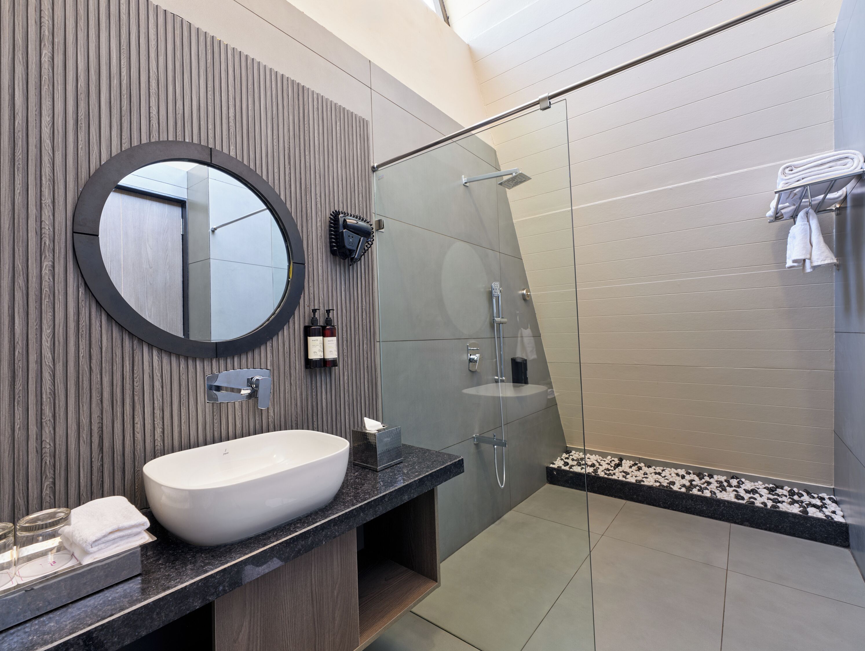 Une salle de bain moderne avec un miroir rond, un lavabo blanc et une douche à parois de verre.