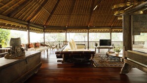 Amplia habitación con techo alto, cama, televisor y zona de estar con vistas al exterior.
