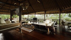 Amplio salón de planta abierta con suelo y muebles de madera, grandes ventanales que ofrecen vistas a exuberante vegetación.