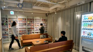 A library with bookshelves, a sofa, a vending machine, and an emergency ladder sign. - Hotel Plus Hostel TOKYO KAWASAKI (Kawasaki)
