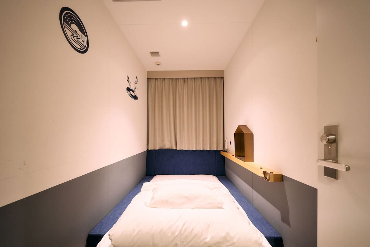 A modern hotel room with a bed, a headboard, a bedside table, a mirror, and a door.