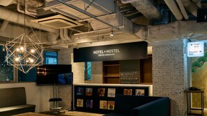 A hotel reception area with a modern design, including a geometric light fixture, a reception desk, and a wall displaying various items. - Hotel Plus Hostel TOKYO KAWASAKI (Kawasaki)
