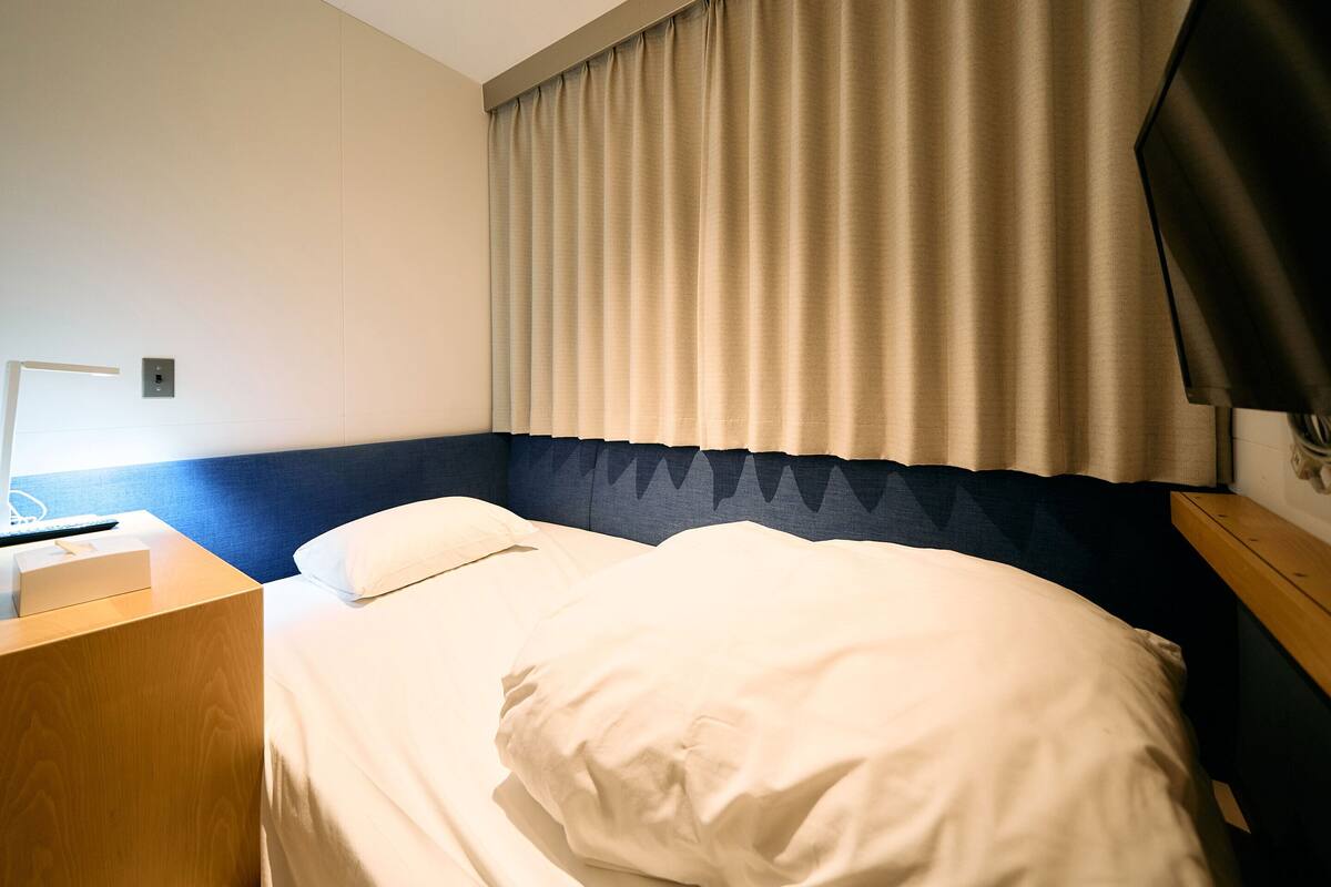 A hotel room with a bed, a bedside table, a lamp, and a window with curtains.