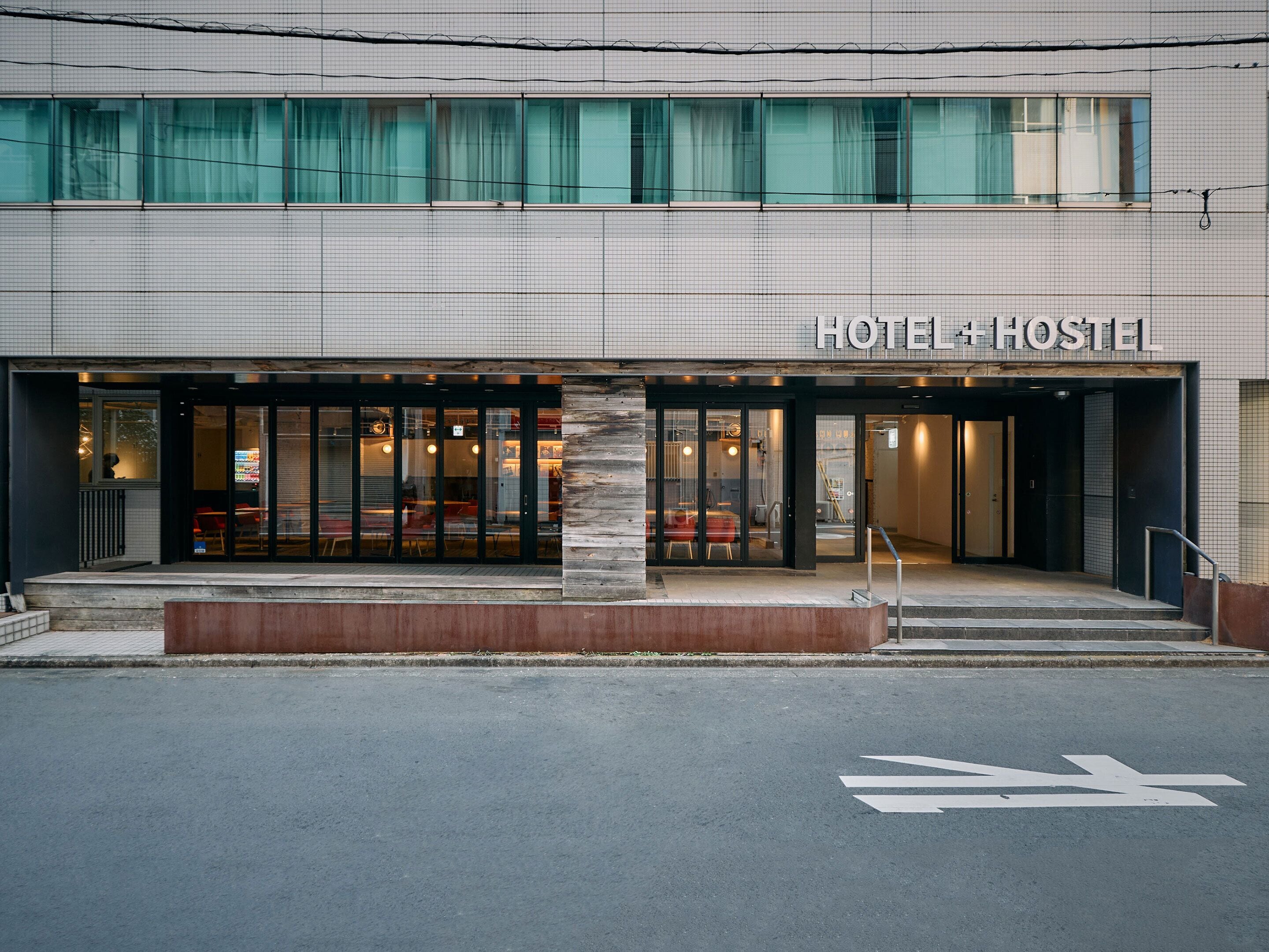 Un hôtel à la façade moderne, doté de grandes fenêtres en verre et d’une enseigne indiquant « HÔTEL + AUBERGE ».