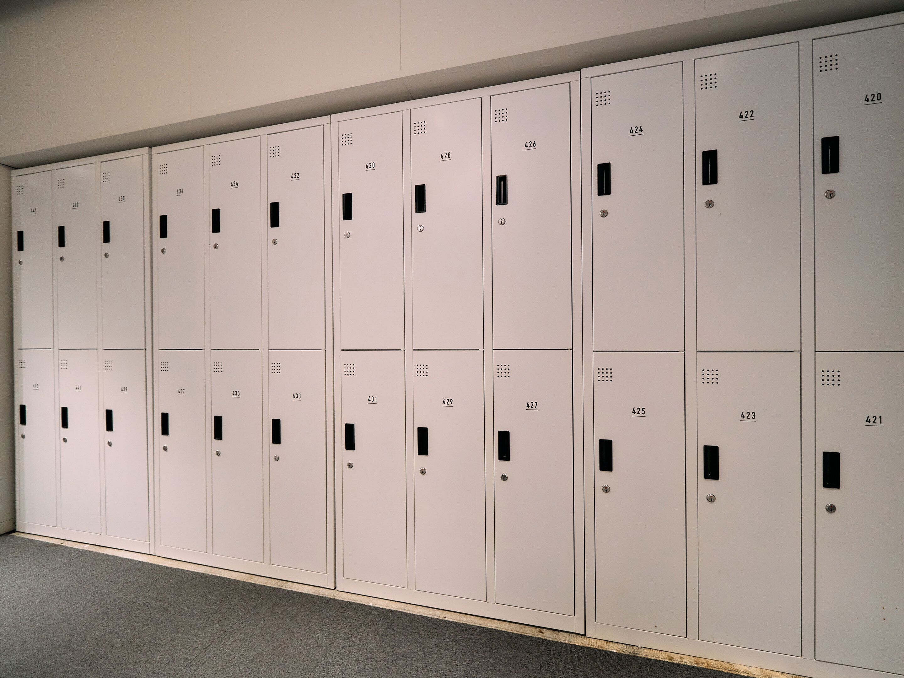 A row of white lockers with numbers on them, arranged in a hallway.