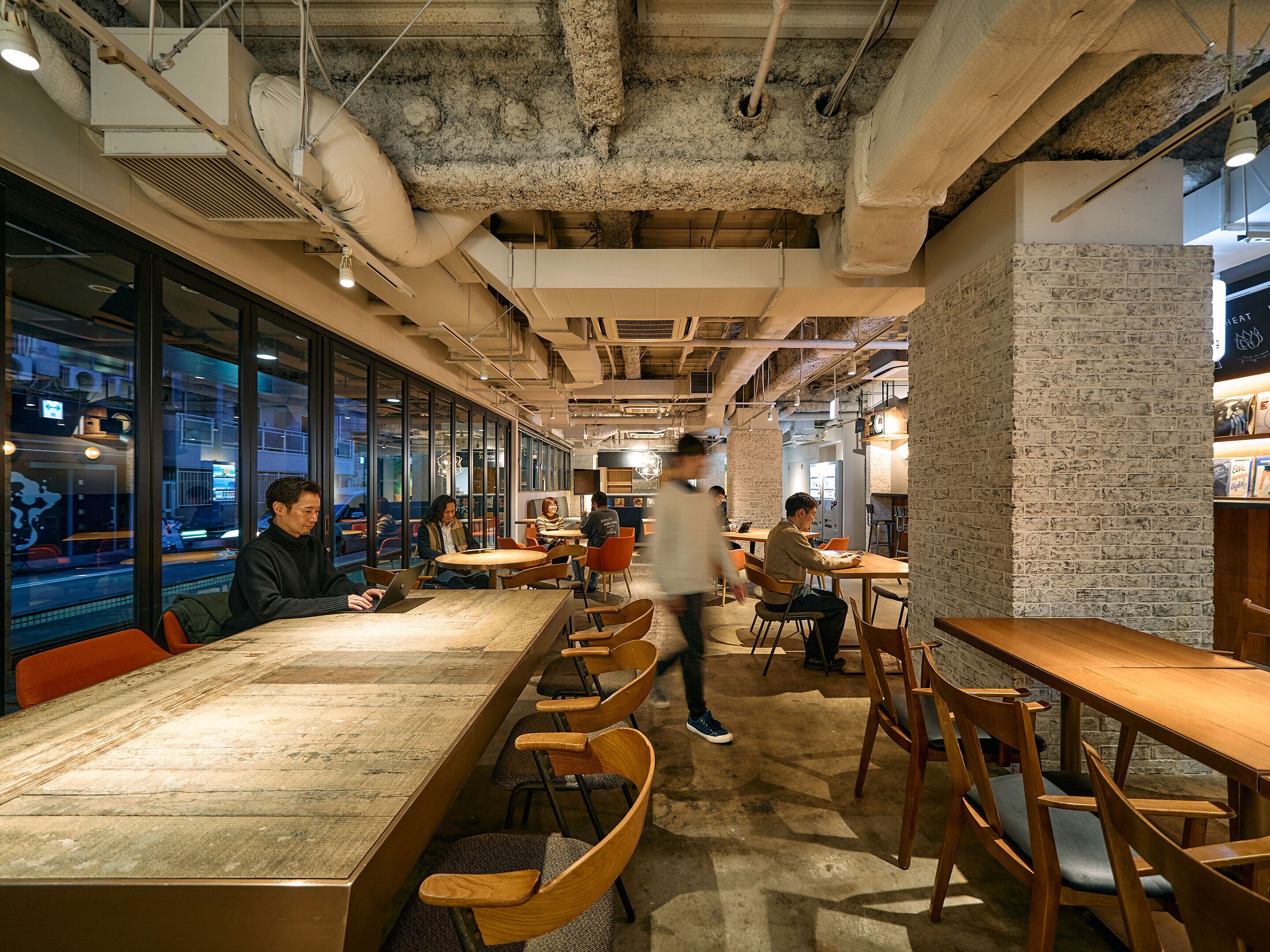 Um espaço moderno de coworking com mesas longas, assentos confortáveis e amplas janelas com vista para a rua.