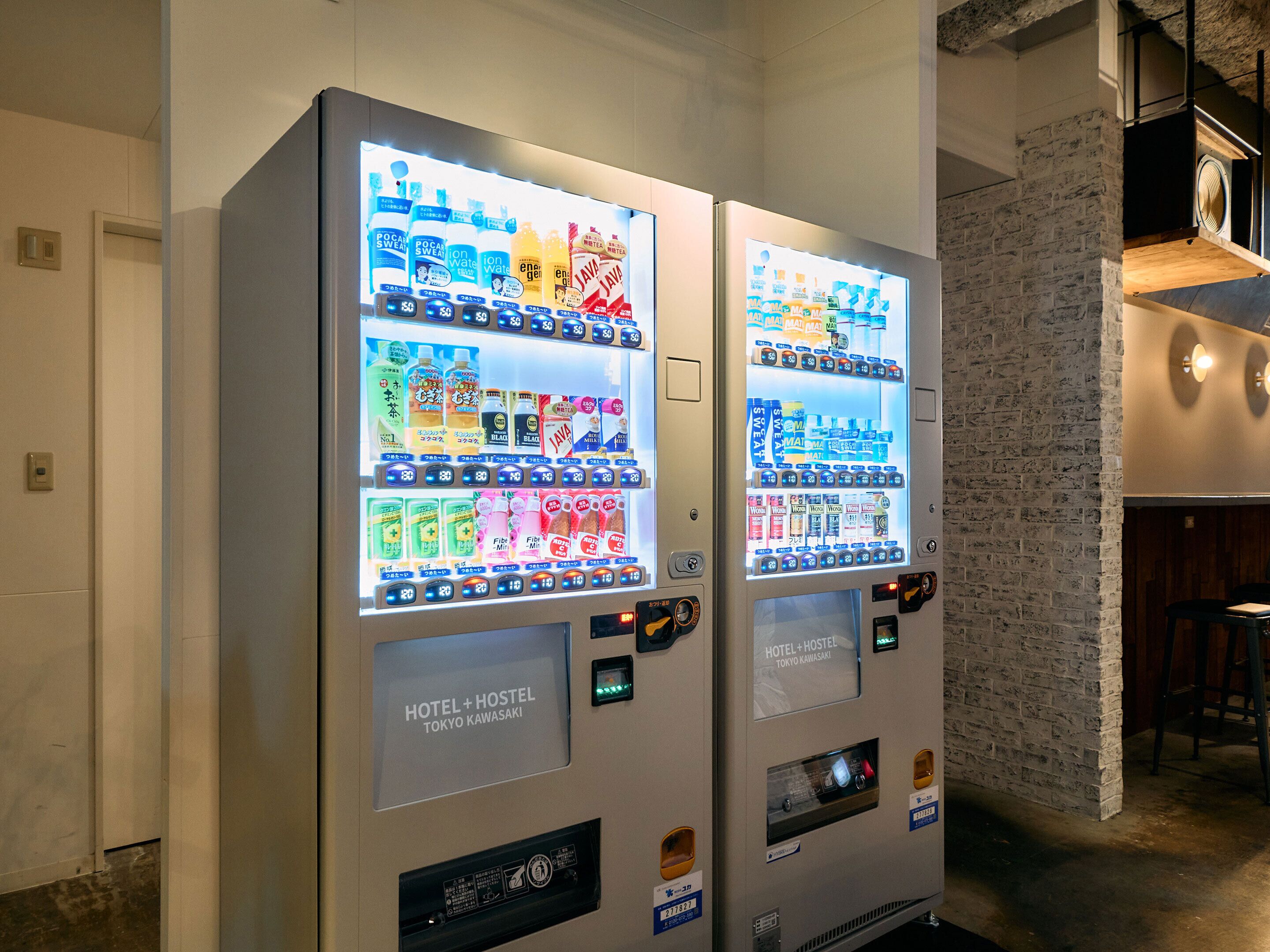 Zwei Getränkeautomaten in einem Hotel, im Hintergrund eine Ziegelwand und eine Bar.