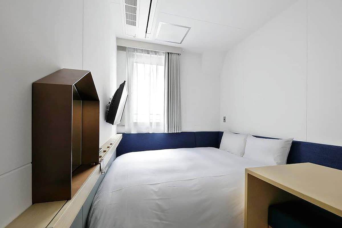 A hotel room with a bed, a desk, a TV, and a window with curtains.