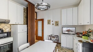 A compact kitchen with white cabinets, a stove, a microwave, a refrigerator, a dining table, and a television.