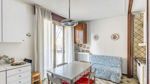 A compact kitchen with a dining table, chairs, a small stool, and a patterned sofa.
