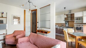 Un salon moderne avec un canapé rose, un coin repas avec une table et des chaises en bois, et une cuisine avec des meubles blancs et une cuisinière.