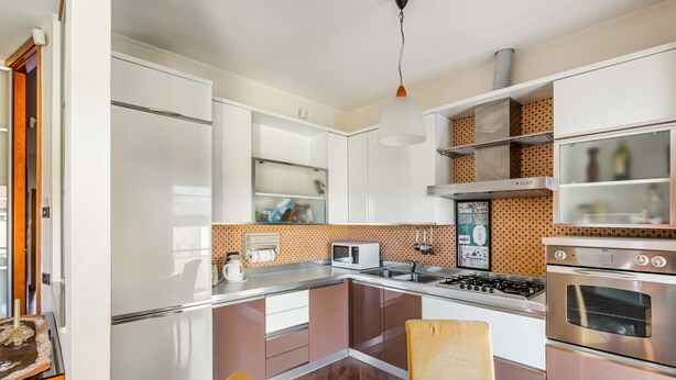 Une cuisine moderne avec des meubles blancs, une cuisinière à gaz, un four à micro-ondes et un réfrigérateur.