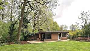 Una casa moderna amb un pati, envoltada d'un jardí ben cuidat i arbres.