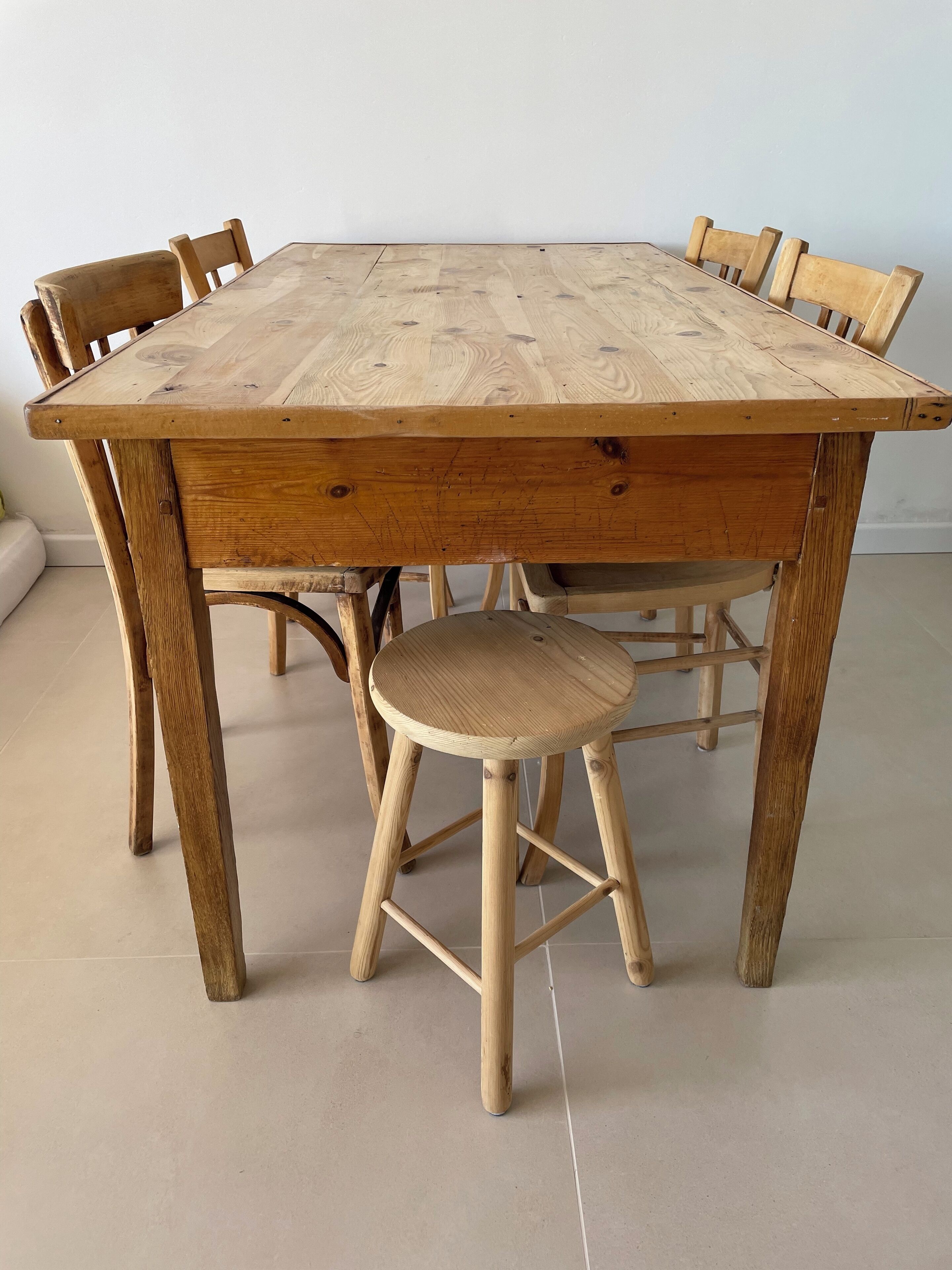 Een houten eettafel met zes stoelen, een rond krukje en een betegelde vloer.