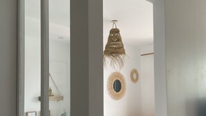 Une chambre avec une grande fenêtre, un lit recouvert d’une courtepointe à rayures bleues et blanches, une commode en bois et deux miroirs fixés au mur.