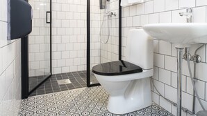A modern bathroom with a glass-enclosed shower, a white toilet, and a sink with a glass shelf. - Hotelli Ville (Tampere)