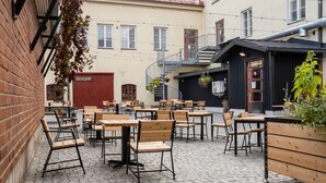 An outdoor café with wooden tables and chairs, a brick wall, and a red door. - Hotelli Ville (Tampere)