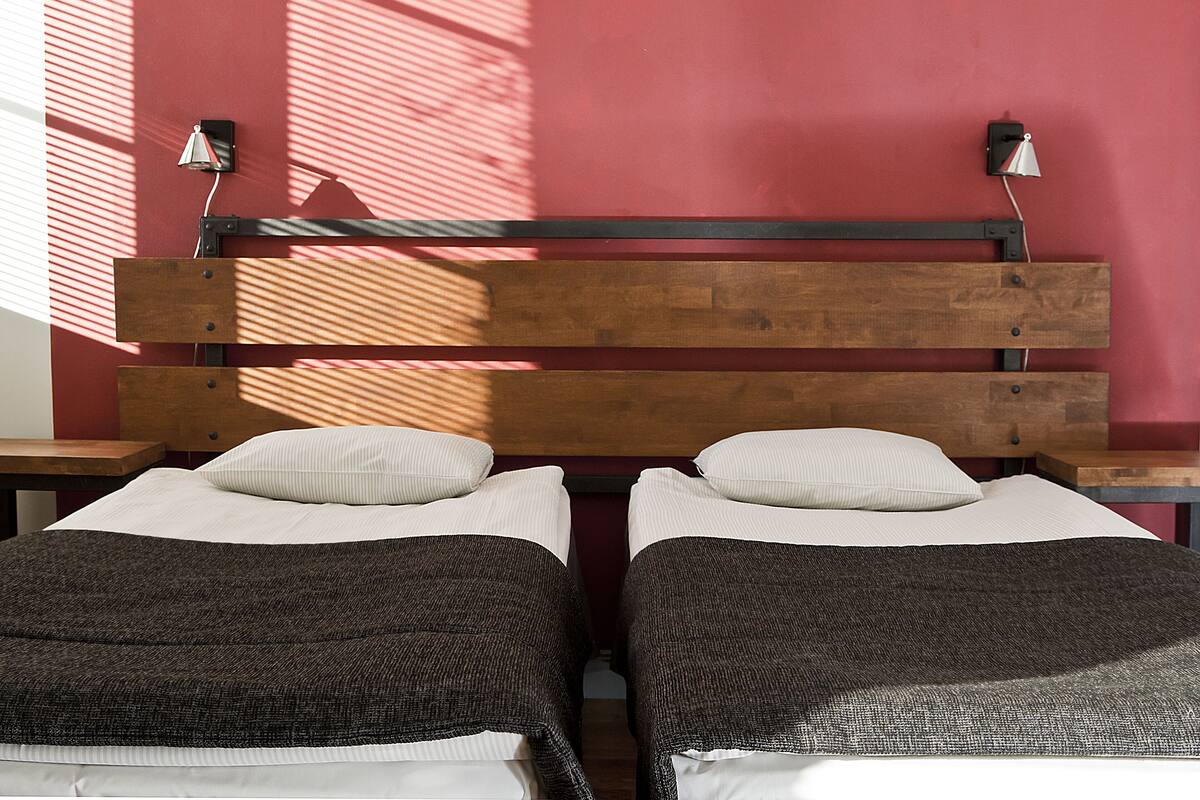 A room with two beds, each with a wooden headboard and a bedside table.