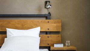A neatly made bed with white and gray bedding, a wooden headboard, a bedside table with a lamp, and a glass of water. - Hotelli Ville (Tampere)